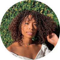 a woman with curly hair posing in front of a hedge