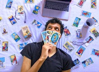 a man holding tarot cards in front of a laptop